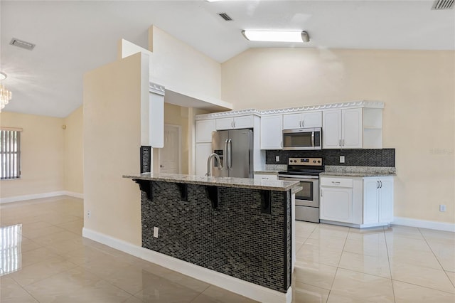 kitchen with white cabinetry, stainless steel appliances, backsplash, lofted ceiling, and a kitchen bar