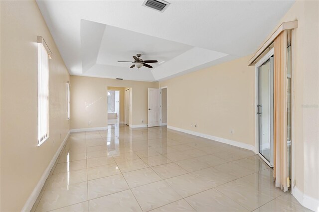 unfurnished room with ceiling fan, a wealth of natural light, and a tray ceiling