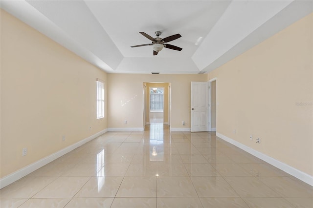 empty room featuring a raised ceiling, ceiling fan, and light tile patterned floors