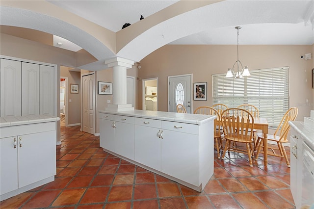 kitchen with vaulted ceiling, ornate columns, decorative light fixtures, white cabinetry, and a chandelier