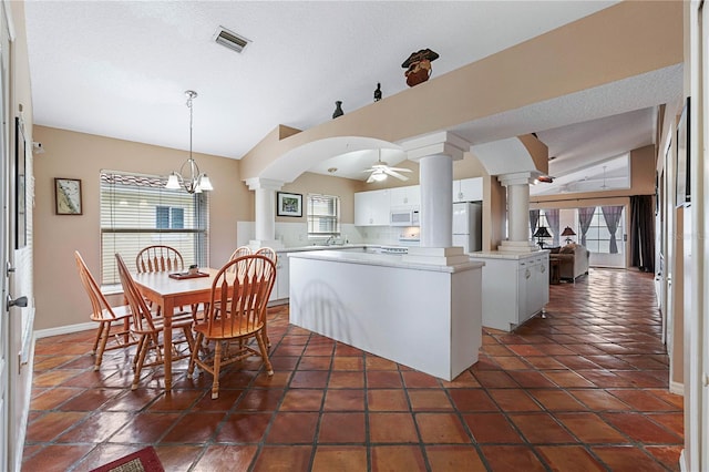 kitchen with white appliances, white cabinets, ceiling fan with notable chandelier, vaulted ceiling, and a kitchen island