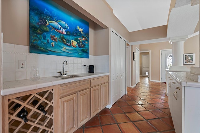 bar featuring light brown cabinets, dark tile patterned flooring, sink, ornate columns, and tile counters