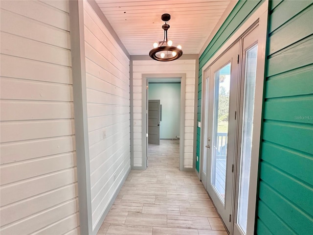 hallway with a chandelier, light hardwood / wood-style flooring, wooden walls, and wood ceiling