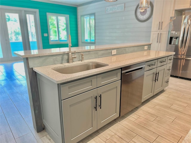 kitchen featuring light stone countertops, gray cabinetry, stainless steel appliances, a kitchen island with sink, and sink