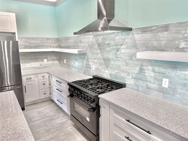 kitchen featuring white cabinets, wall chimney exhaust hood, light stone counters, and stainless steel appliances