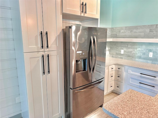 kitchen featuring light stone countertops, stainless steel refrigerator with ice dispenser, tasteful backsplash, and white cabinetry