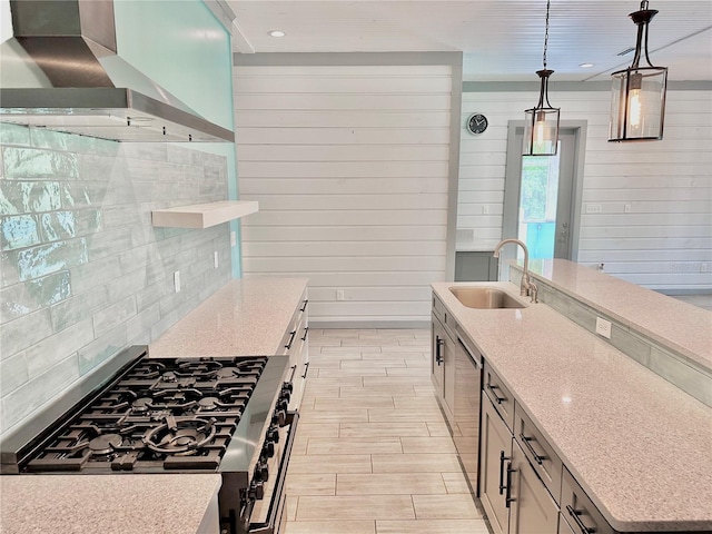 kitchen featuring light stone counters, wall chimney exhaust hood, stainless steel gas range, sink, and pendant lighting