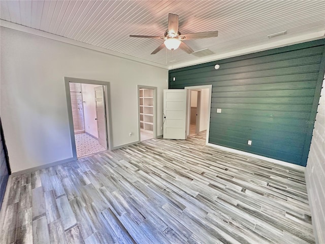 unfurnished bedroom featuring ensuite bath, ceiling fan, light hardwood / wood-style flooring, and wooden walls