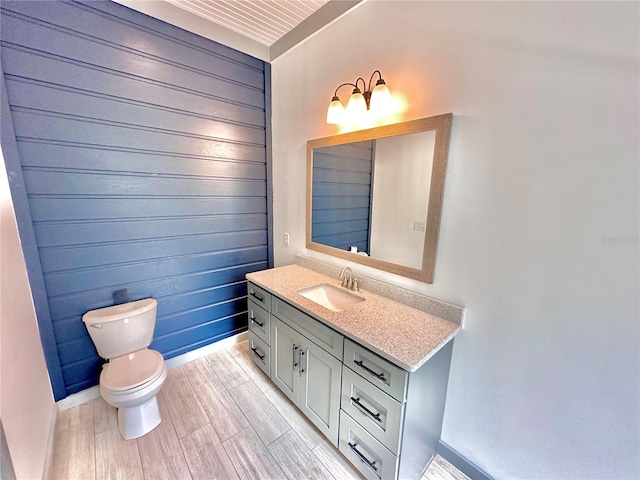 bathroom with vanity, toilet, wood-type flooring, and wooden walls