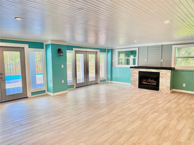 unfurnished living room with wooden walls, french doors, a wealth of natural light, and light hardwood / wood-style flooring