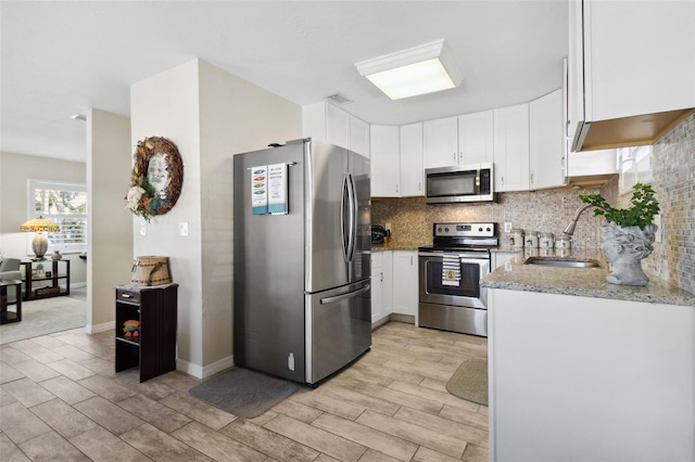 kitchen with white cabinets, sink, light wood-type flooring, light stone countertops, and appliances with stainless steel finishes