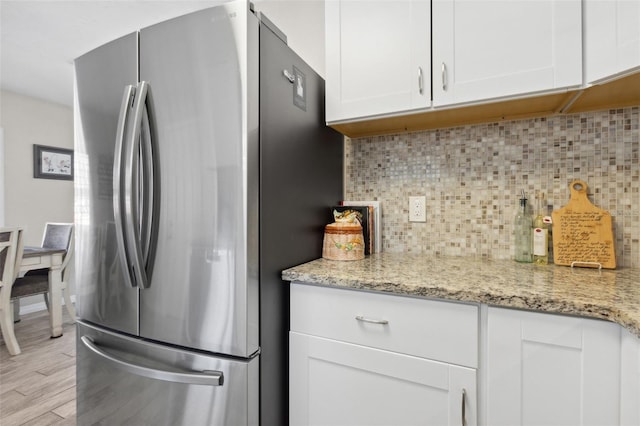 kitchen featuring white cabinets, stainless steel fridge, light hardwood / wood-style flooring, and light stone countertops