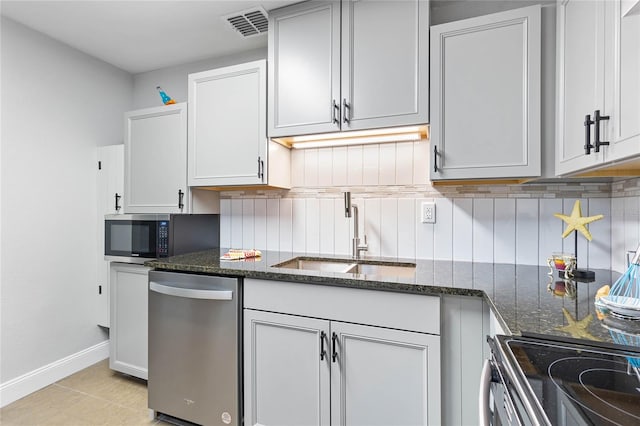 kitchen featuring sink, stainless steel appliances, tasteful backsplash, dark stone counters, and light tile patterned floors