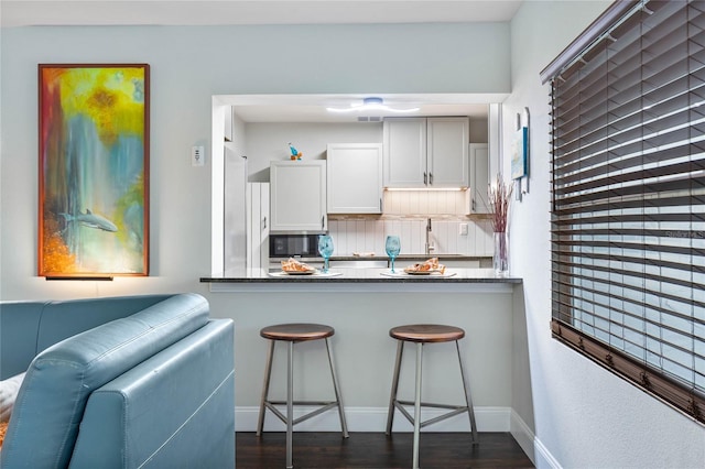 kitchen featuring a kitchen bar, dark hardwood / wood-style flooring, backsplash, stone counters, and white cabinets