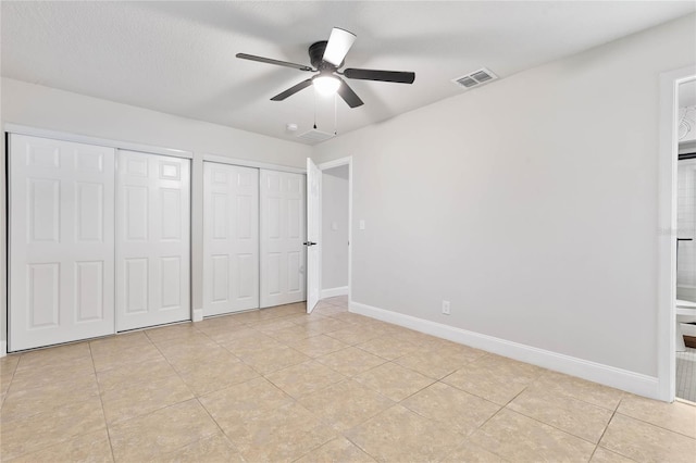 unfurnished bedroom with light tile patterned floors, a textured ceiling, two closets, and ceiling fan