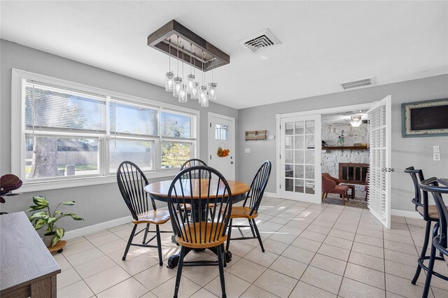 tiled dining room with a fireplace, a chandelier, and french doors