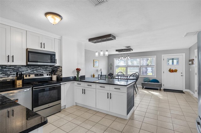 kitchen featuring white cabinets, hanging light fixtures, appliances with stainless steel finishes, tasteful backsplash, and kitchen peninsula