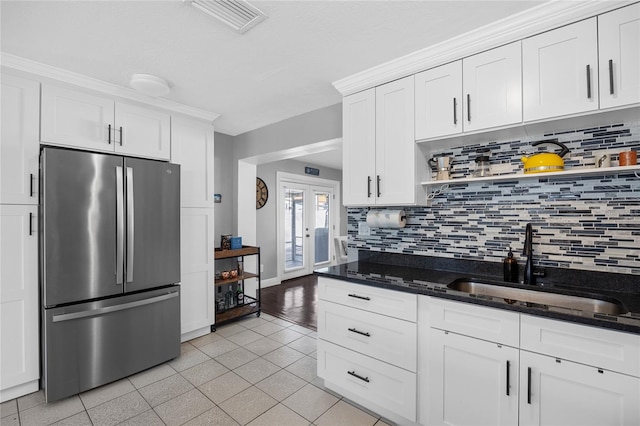 kitchen with french doors, white cabinets, dark stone countertops, tasteful backsplash, and stainless steel refrigerator