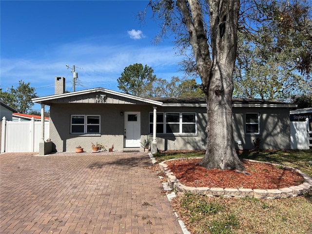 ranch-style home with a chimney, fence, and stucco siding