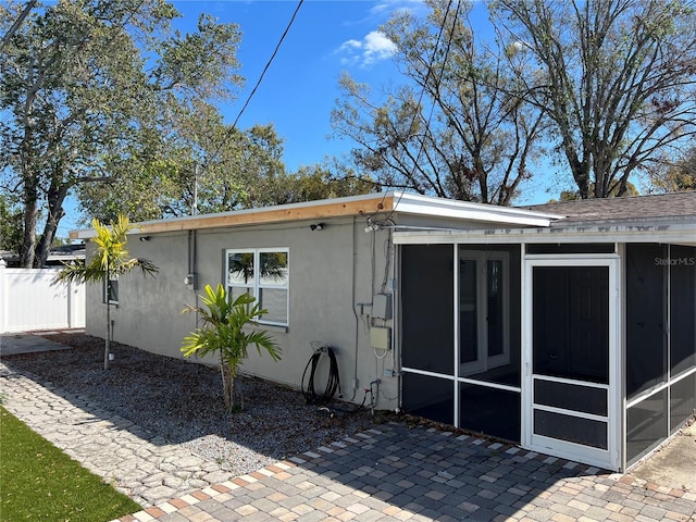 rear view of property with a sunroom, fence, and stucco siding