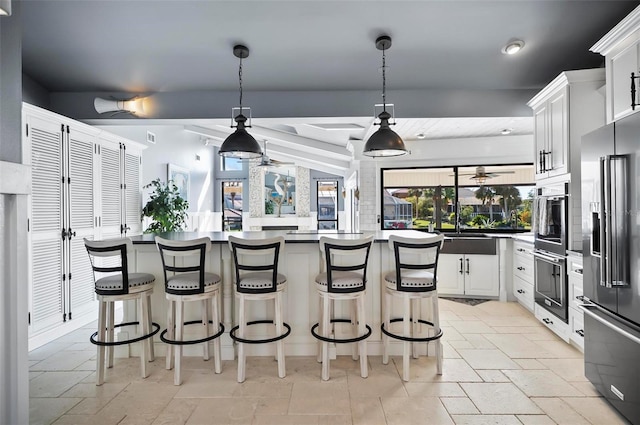 kitchen with beam ceiling, white cabinetry, hanging light fixtures, stainless steel appliances, and a kitchen bar