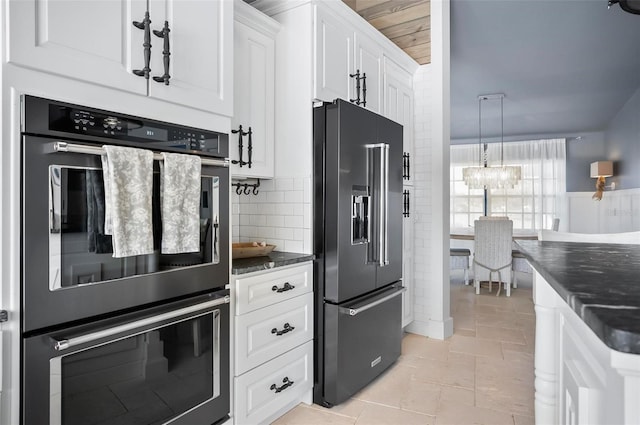 kitchen featuring appliances with stainless steel finishes, backsplash, dark stone counters, white cabinetry, and hanging light fixtures