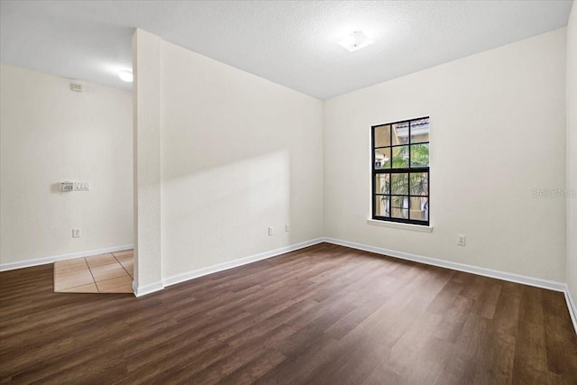 spare room with a textured ceiling, baseboards, and wood finished floors