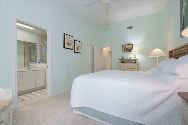 bedroom with ceiling fan, light colored carpet, and ensuite bath