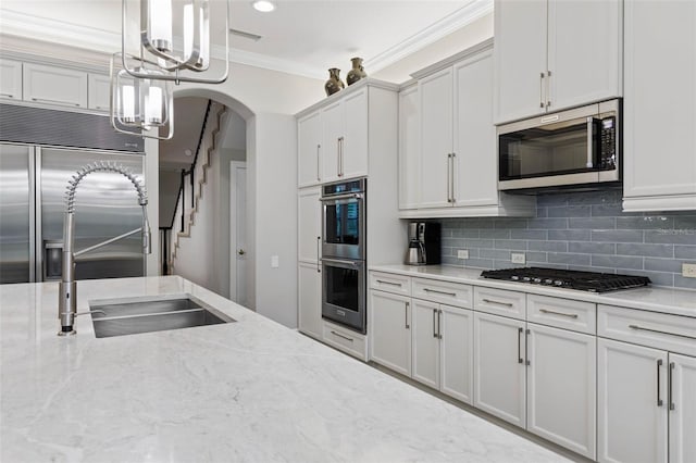 kitchen featuring backsplash, white cabinets, crown molding, light stone countertops, and stainless steel appliances