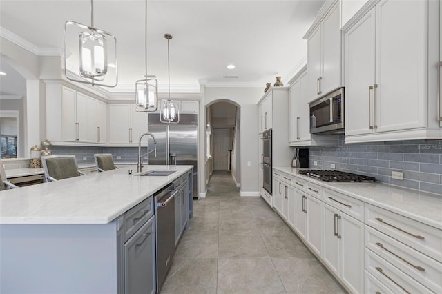 kitchen featuring pendant lighting, backsplash, white cabinets, a center island with sink, and stainless steel appliances