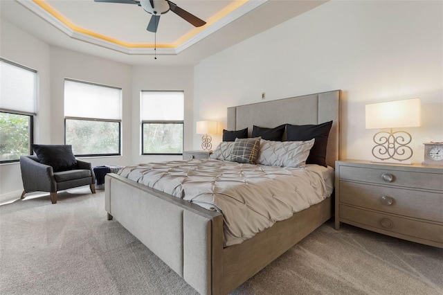 carpeted bedroom with a raised ceiling, ceiling fan, and crown molding