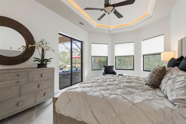 carpeted bedroom featuring a tray ceiling, access to exterior, and ceiling fan