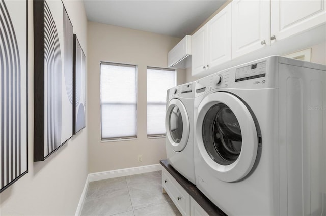 clothes washing area with washing machine and dryer, light tile patterned floors, and cabinets