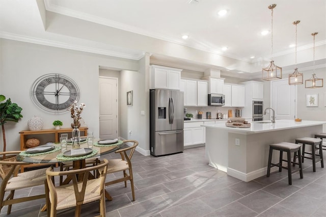 kitchen with a center island with sink, a kitchen breakfast bar, white cabinets, hanging light fixtures, and stainless steel appliances