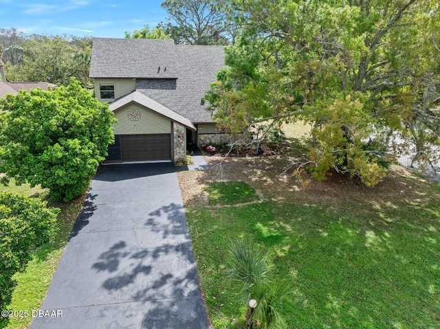 view of front of house featuring an attached garage, a shingled roof, a front lawn, stone siding, and driveway