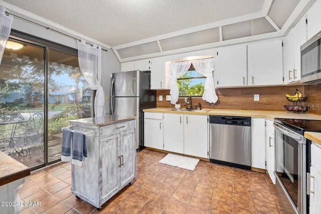 kitchen with lofted ceiling, a sink, light countertops, white cabinets, and appliances with stainless steel finishes