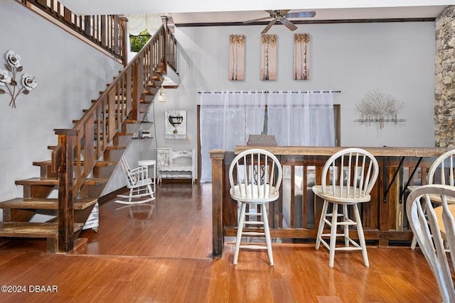 unfurnished dining area featuring a ceiling fan, wood finished floors, bar area, a towering ceiling, and stairs