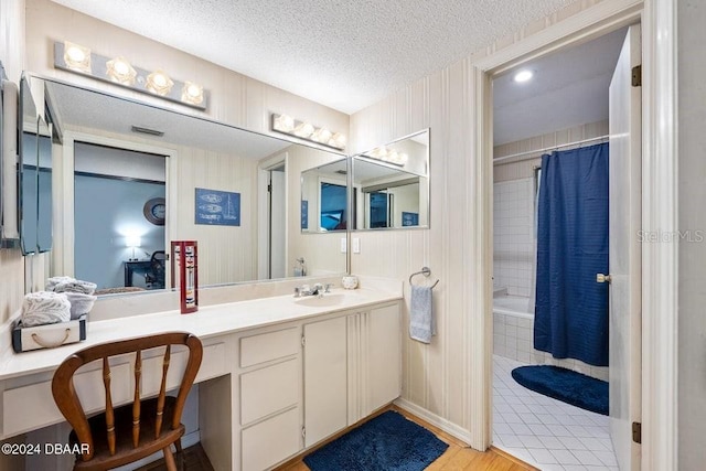 bathroom with a textured ceiling, vanity, and tiled shower / bath combo