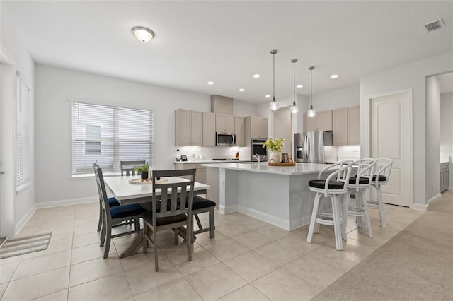 kitchen featuring gray cabinetry, hanging light fixtures, stainless steel appliances, an island with sink, and light tile patterned floors