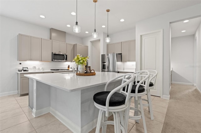 kitchen with gray cabinetry, a kitchen island with sink, hanging light fixtures, light tile patterned floors, and stainless steel appliances