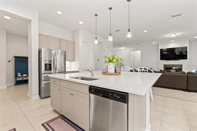 kitchen with sink, pendant lighting, a tiled fireplace, a center island with sink, and appliances with stainless steel finishes