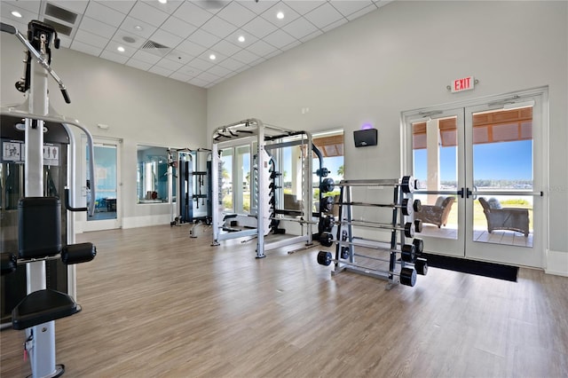 gym featuring a drop ceiling, a towering ceiling, light hardwood / wood-style floors, and french doors