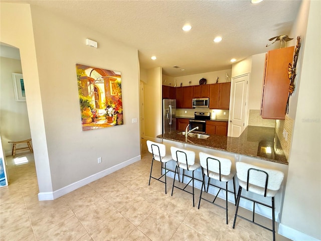 kitchen with a kitchen bar, a textured ceiling, stainless steel appliances, and kitchen peninsula