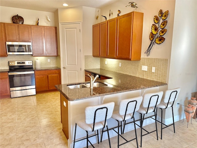 kitchen with kitchen peninsula, appliances with stainless steel finishes, a kitchen breakfast bar, and sink