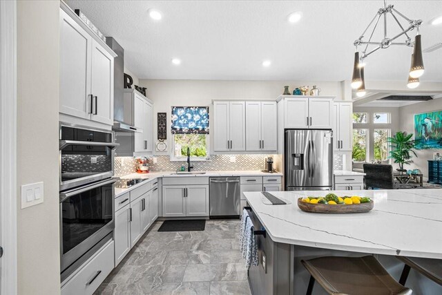 kitchen featuring sink, tasteful backsplash, decorative light fixtures, light stone counters, and stainless steel appliances