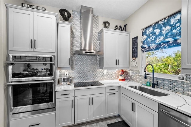 kitchen featuring sink, wall chimney exhaust hood, light stone countertops, tasteful backsplash, and stainless steel appliances