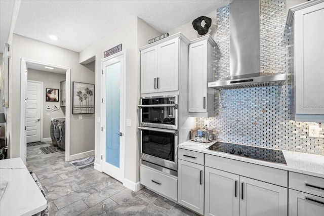 kitchen featuring wall chimney exhaust hood, separate washer and dryer, black electric cooktop, double oven, and tasteful backsplash