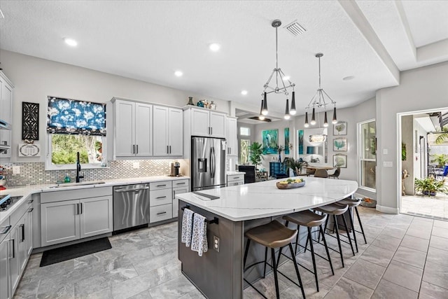 kitchen with a kitchen bar, appliances with stainless steel finishes, sink, pendant lighting, and a center island