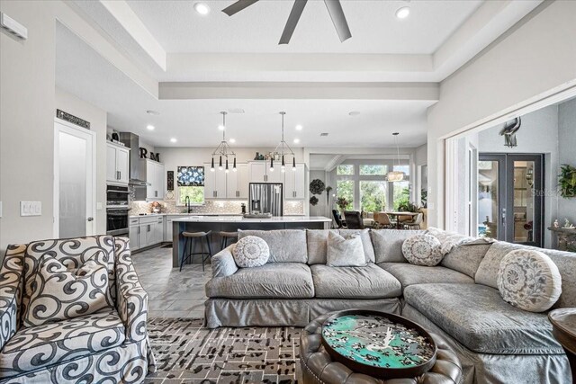 living room with ceiling fan with notable chandelier, french doors, sink, and a tray ceiling