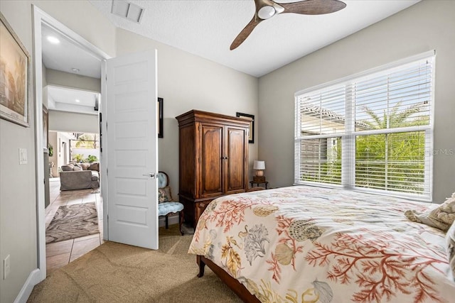 bedroom with ceiling fan, light colored carpet, and a textured ceiling